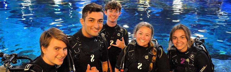 四名学生在潜水前戴着潜水服微笑