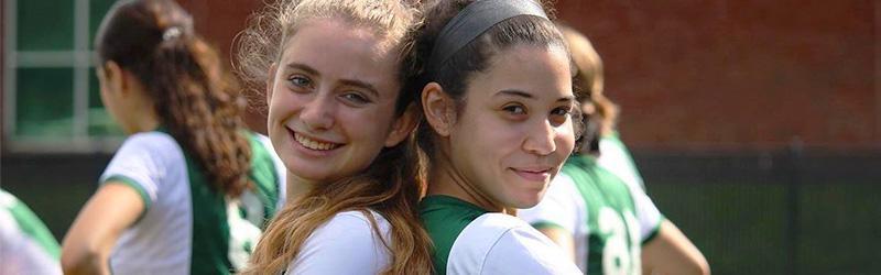 两个女孩穿着足球服背靠背微笑着 
